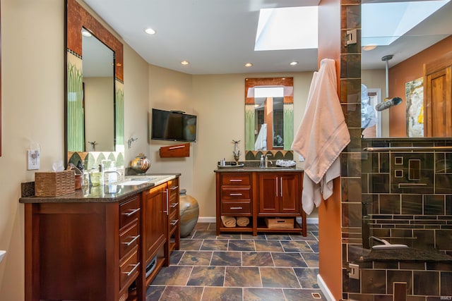 bathroom with a skylight, recessed lighting, two vanities, a sink, and a tile shower