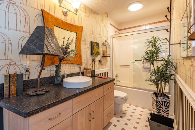 full bath with a textured ceiling, toilet, bath / shower combo with glass door, vanity, and wallpapered walls