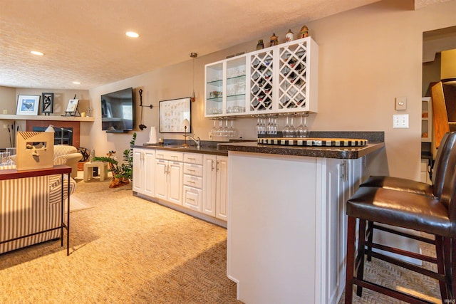 kitchen featuring dark countertops, a kitchen bar, white cabinets, and a sink