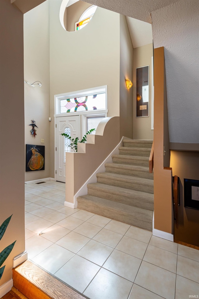 foyer entrance featuring a towering ceiling, stairs, baseboards, and light tile patterned flooring