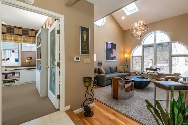 interior space featuring a skylight, baseboards, light wood-style flooring, high vaulted ceiling, and a notable chandelier