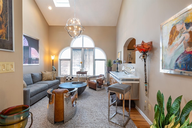 living room with high vaulted ceiling, a skylight, baseboards, and an inviting chandelier