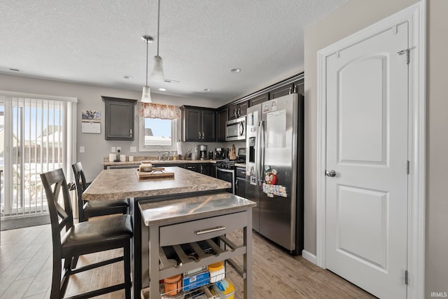 kitchen with light wood-style flooring, a kitchen island, hanging light fixtures, appliances with stainless steel finishes, and dark brown cabinets