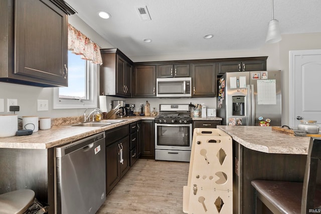 kitchen featuring light countertops, hanging light fixtures, appliances with stainless steel finishes, a sink, and dark brown cabinetry