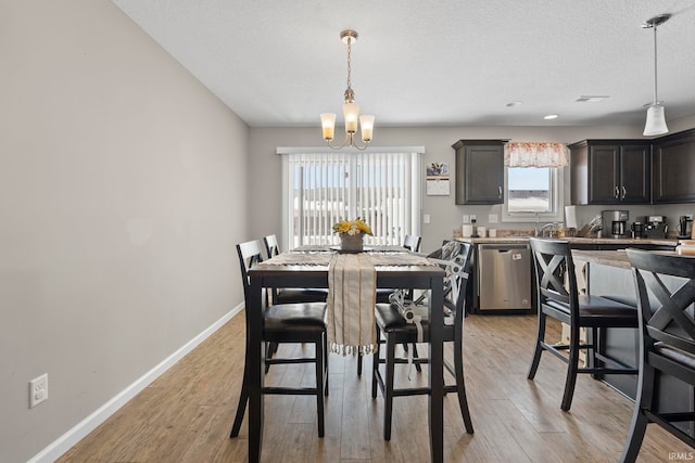 dining space with light wood-style floors, a textured ceiling, baseboards, and a notable chandelier