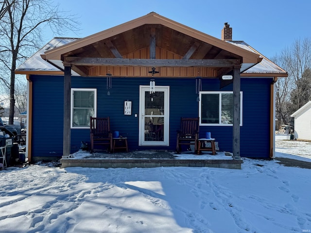 bungalow-style home with covered porch, a chimney, and metal roof