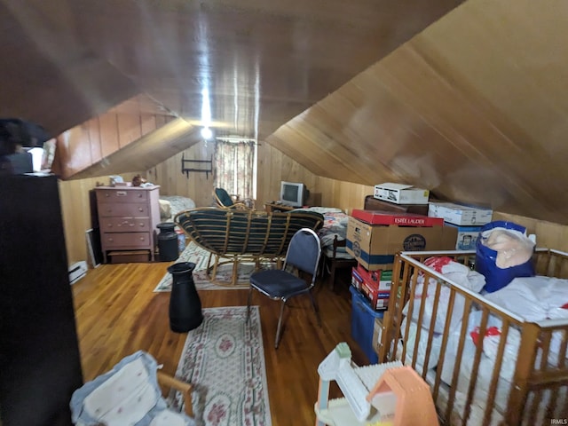 bedroom with lofted ceiling, wooden walls, a baseboard heating unit, and wood finished floors