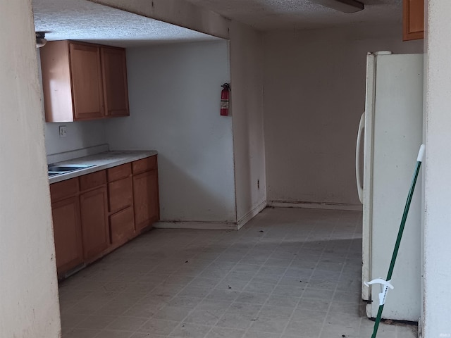 kitchen featuring light countertops, light floors, freestanding refrigerator, and brown cabinets