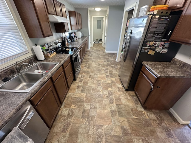 kitchen with baseboards, dark countertops, appliances with stainless steel finishes, under cabinet range hood, and a sink