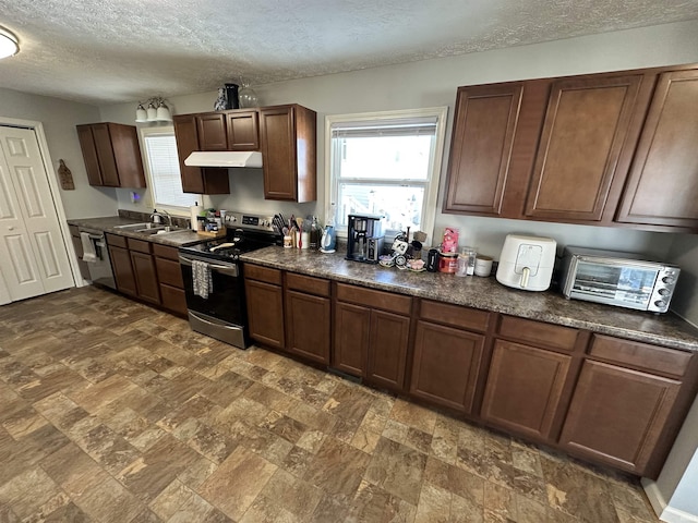 kitchen with a textured ceiling, under cabinet range hood, stainless steel appliances, a sink, and dark countertops