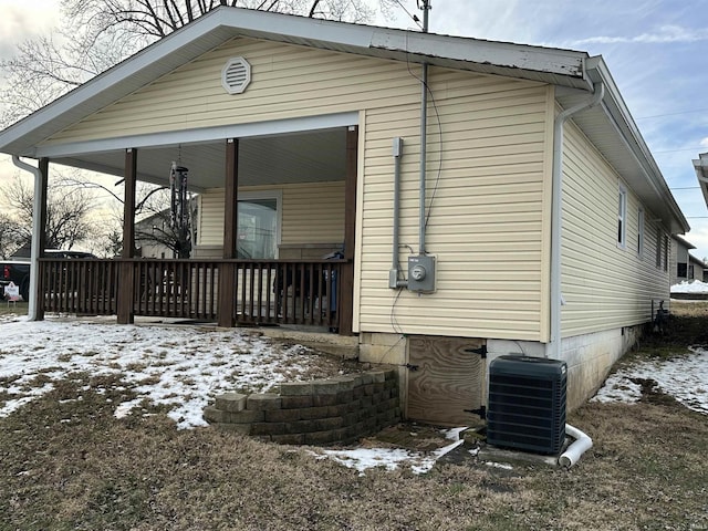 view of snowy exterior with covered porch and central AC unit