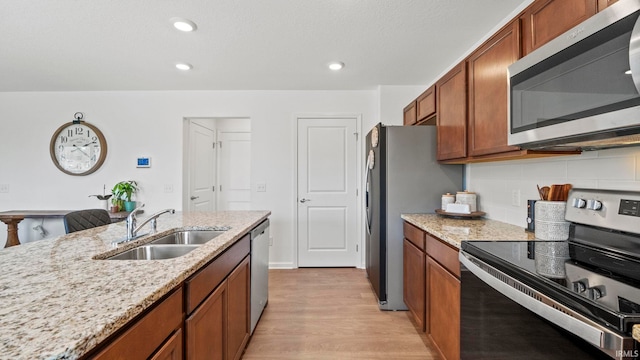 kitchen with appliances with stainless steel finishes, brown cabinets, a sink, and light stone countertops