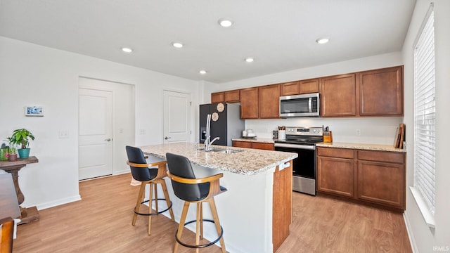 kitchen with appliances with stainless steel finishes, light wood-type flooring, a sink, and a kitchen island with sink