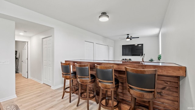 bar featuring baseboards, ceiling fan, light wood-style flooring, and a dry bar