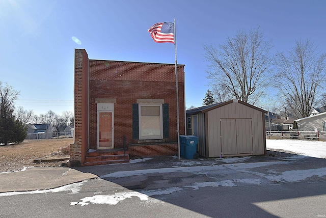 view of front facade featuring entry steps, an outbuilding, brick siding, fence, and a storage unit