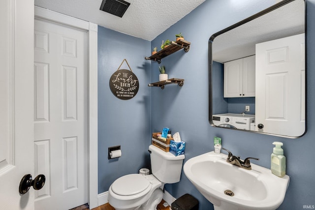 bathroom featuring a textured ceiling, a sink, visible vents, baseboards, and washer / clothes dryer