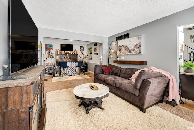 living area with a textured ceiling, light carpet, visible vents, baseboards, and a dry bar