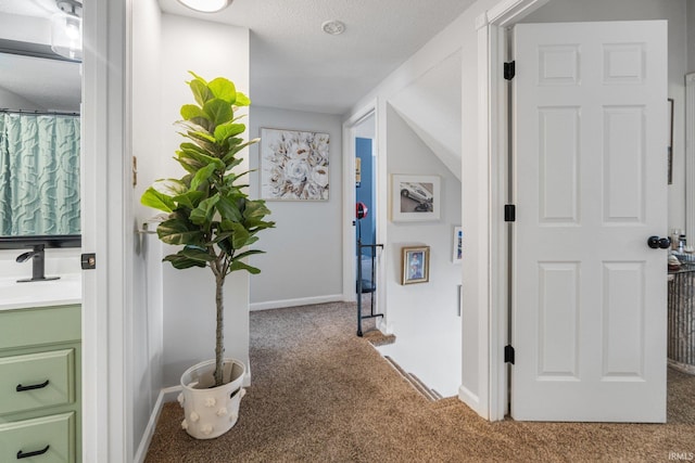 hallway with carpet flooring, a sink, a textured ceiling, and baseboards