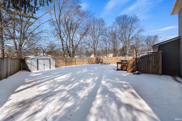 yard layered in snow featuring an outbuilding, a fenced backyard, and a shed