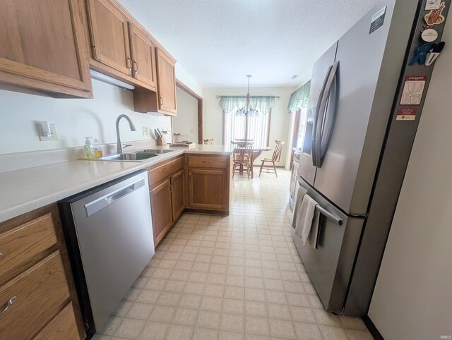 kitchen with appliances with stainless steel finishes, hanging light fixtures, light countertops, light floors, and a sink