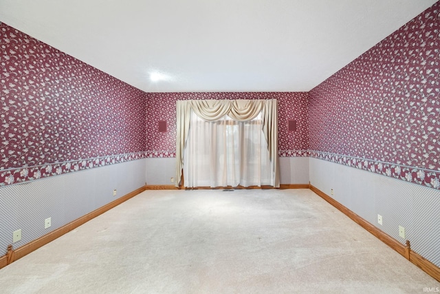 carpeted empty room featuring baseboards and wallpapered walls