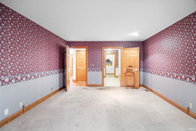 carpeted spare room with a wainscoted wall, baseboards, and wallpapered walls