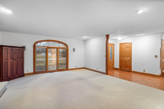 empty room with light carpet, a textured ceiling, and baseboards