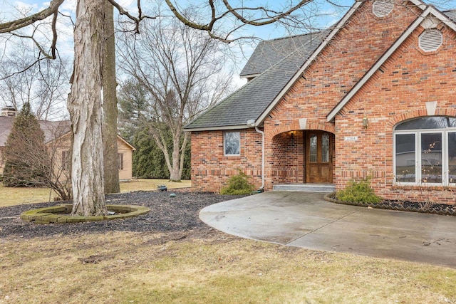 view of front of home with brick siding and roof with shingles