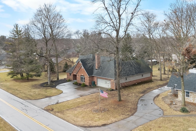 exterior space featuring driveway, a garage, brick siding, a chimney, and a front yard