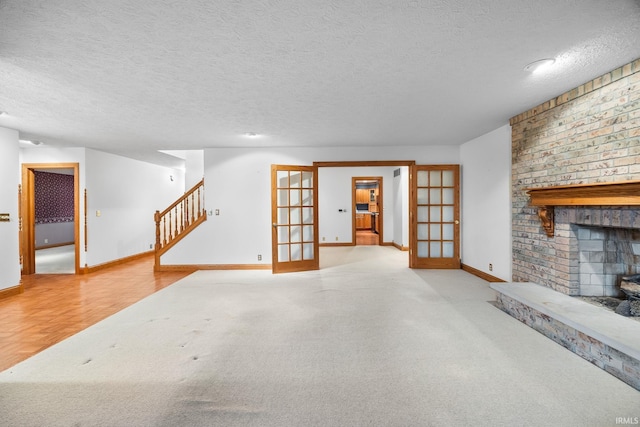 unfurnished living room featuring french doors, a fireplace, a textured ceiling, and stairs