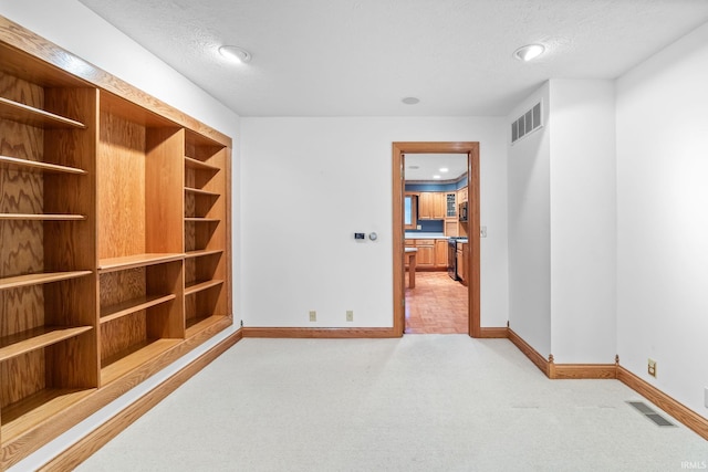 spare room with light colored carpet, visible vents, a textured ceiling, and baseboards