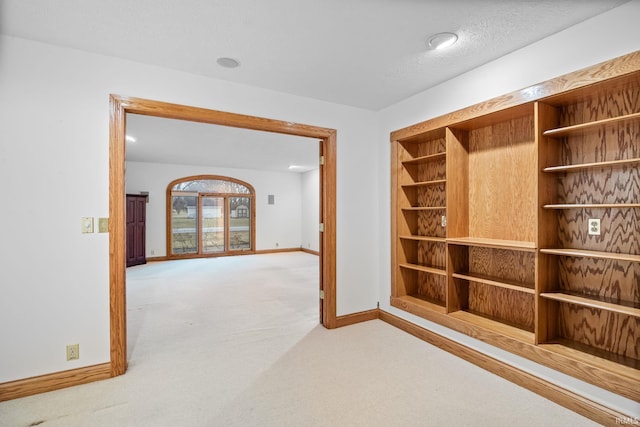 corridor featuring baseboards, a textured ceiling, and light colored carpet