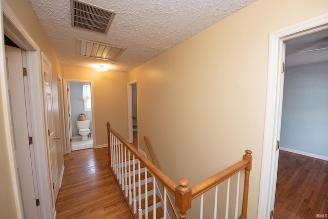 hall featuring visible vents, a textured ceiling, wood finished floors, and an upstairs landing