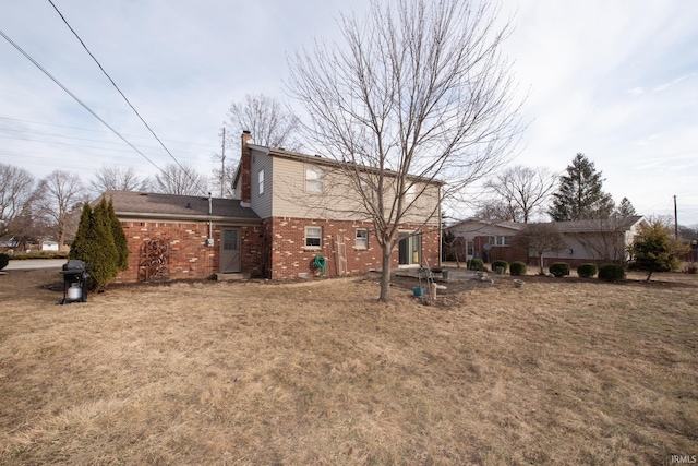 rear view of house featuring brick siding, a lawn, and a chimney