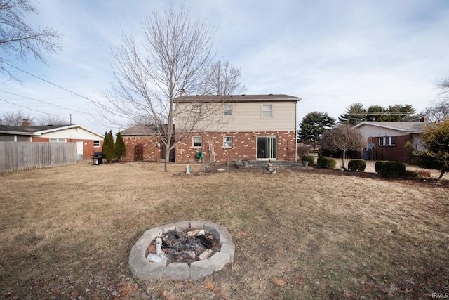 rear view of property featuring a yard, an outdoor fire pit, fence, and brick siding