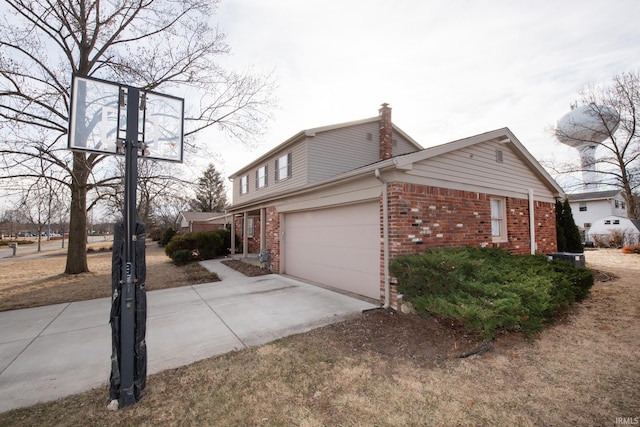 view of side of property featuring a garage, brick siding, driveway, and a chimney