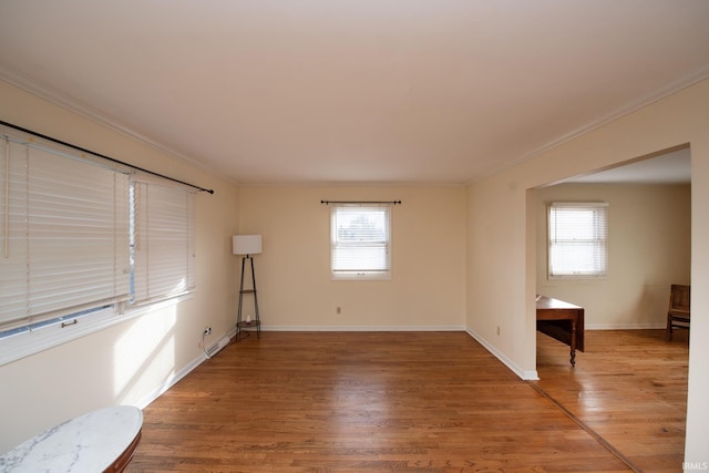 empty room featuring plenty of natural light, crown molding, baseboards, and wood finished floors