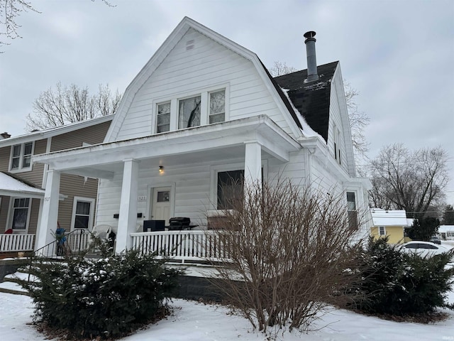 colonial inspired home with a shingled roof, covered porch, and a gambrel roof