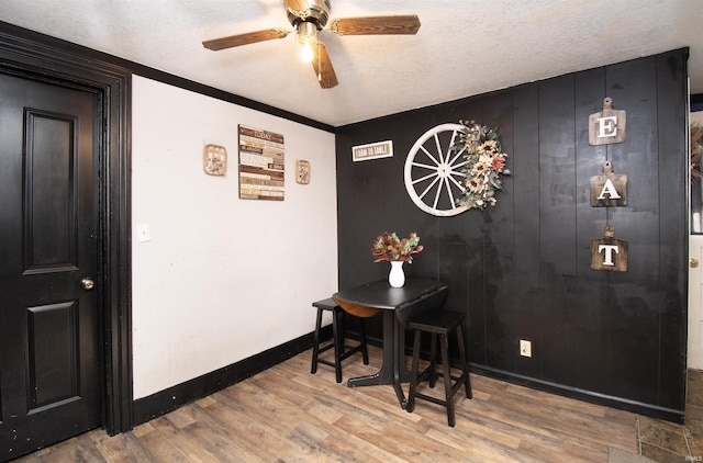 dining space with ceiling fan, a textured ceiling, baseboards, and wood finished floors