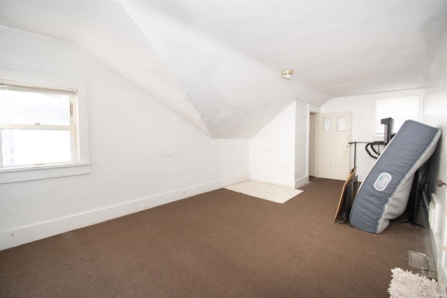 additional living space with baseboards, dark carpet, and vaulted ceiling