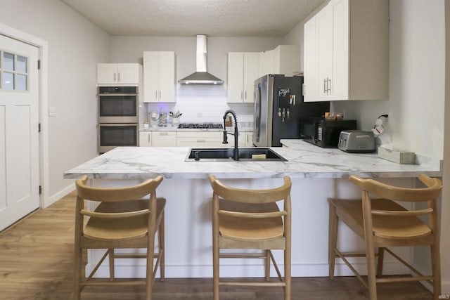 kitchen with wall chimney exhaust hood, appliances with stainless steel finishes, a breakfast bar area, and white cabinets