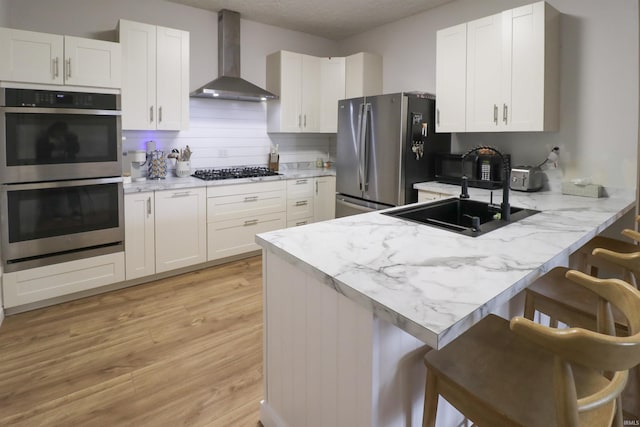 kitchen with stainless steel appliances, a breakfast bar, white cabinetry, and wall chimney exhaust hood