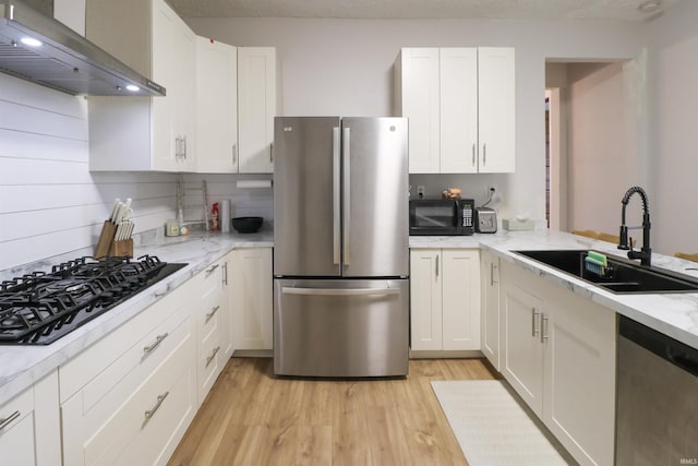 kitchen with white cabinets, wall chimney range hood, stainless steel appliances, and a sink