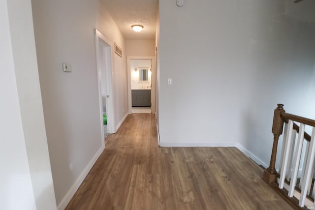 corridor with visible vents, a textured ceiling, baseboards, and wood finished floors