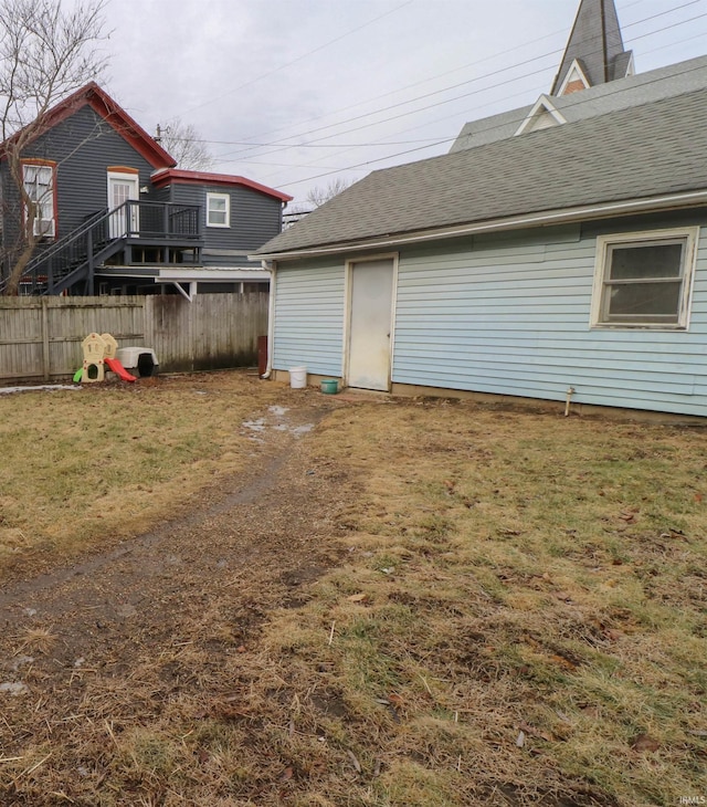 exterior space with a shingled roof, a lawn, and fence