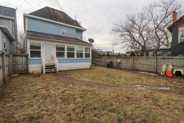 back of house with entry steps, a lawn, and a fenced backyard