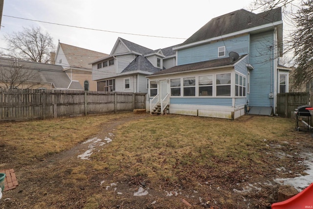 rear view of house with entry steps, a yard, a fenced backyard, and a sunroom