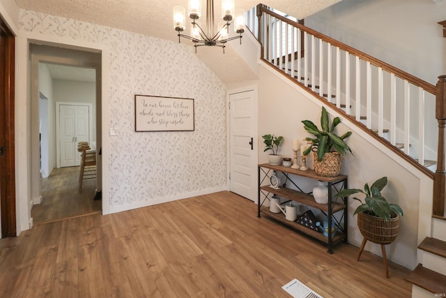 entryway featuring wallpapered walls, a textured ceiling, wood finished floors, baseboards, and stairs