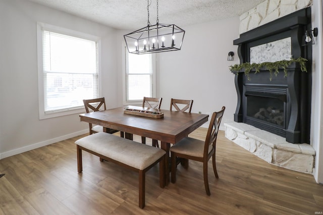 dining area with a textured ceiling, a fireplace, wood finished floors, and baseboards