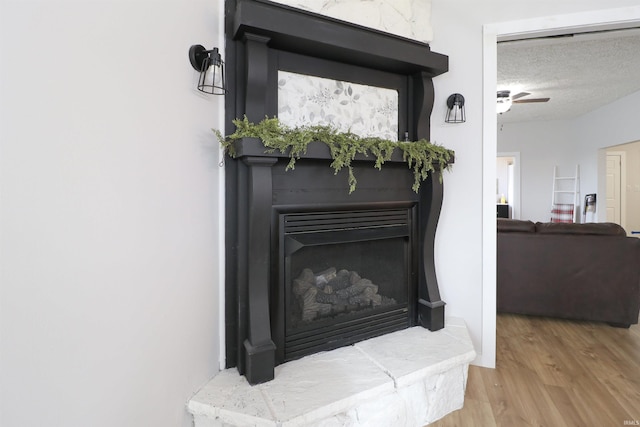 details with ceiling fan, a fireplace with raised hearth, a textured ceiling, and wood finished floors